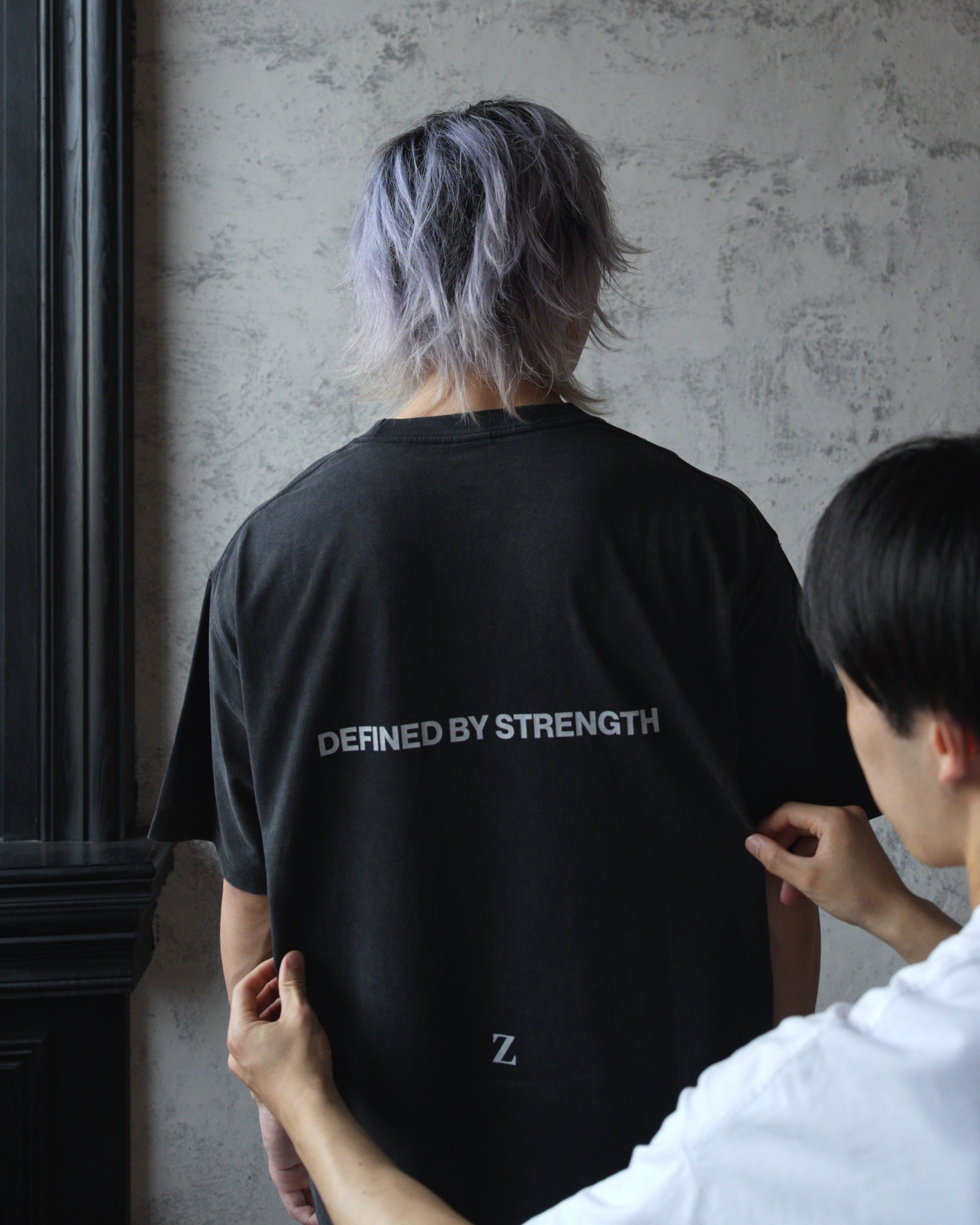 Close-up of Zelos Tee Black back print reading Defined by Strength