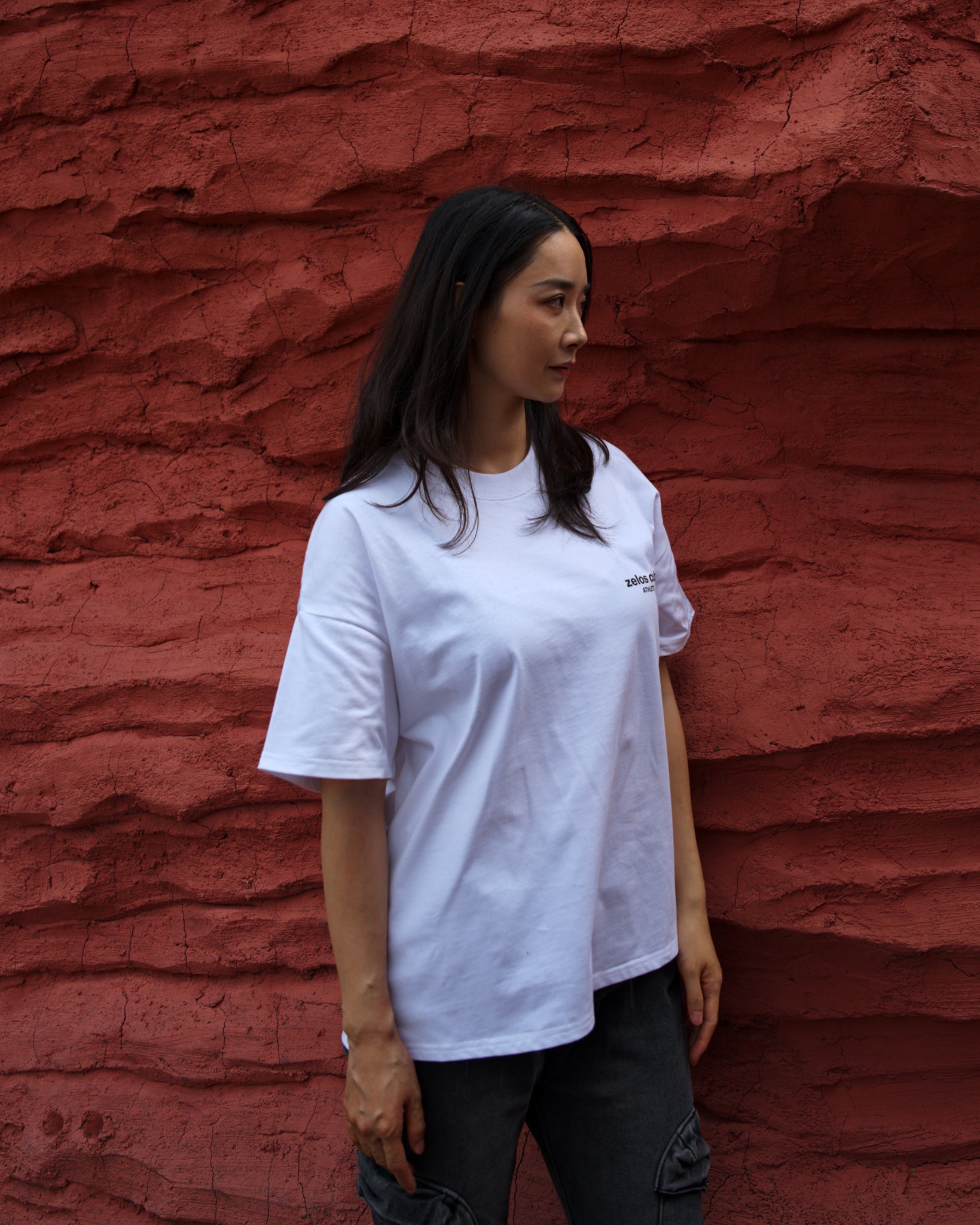 Female model wearing Zelos Tee White, front detail against red rock wall